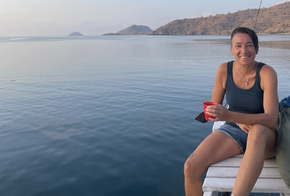 Sarah Simone Degethof is 'the surfing doula' offering her Doula Service to families and new parents. Sarah Simone Degethof sits at the reeling of an anchored boat, holding a cup in her hand and the panoramic scenery of Komodo Island and the ocean in her back.